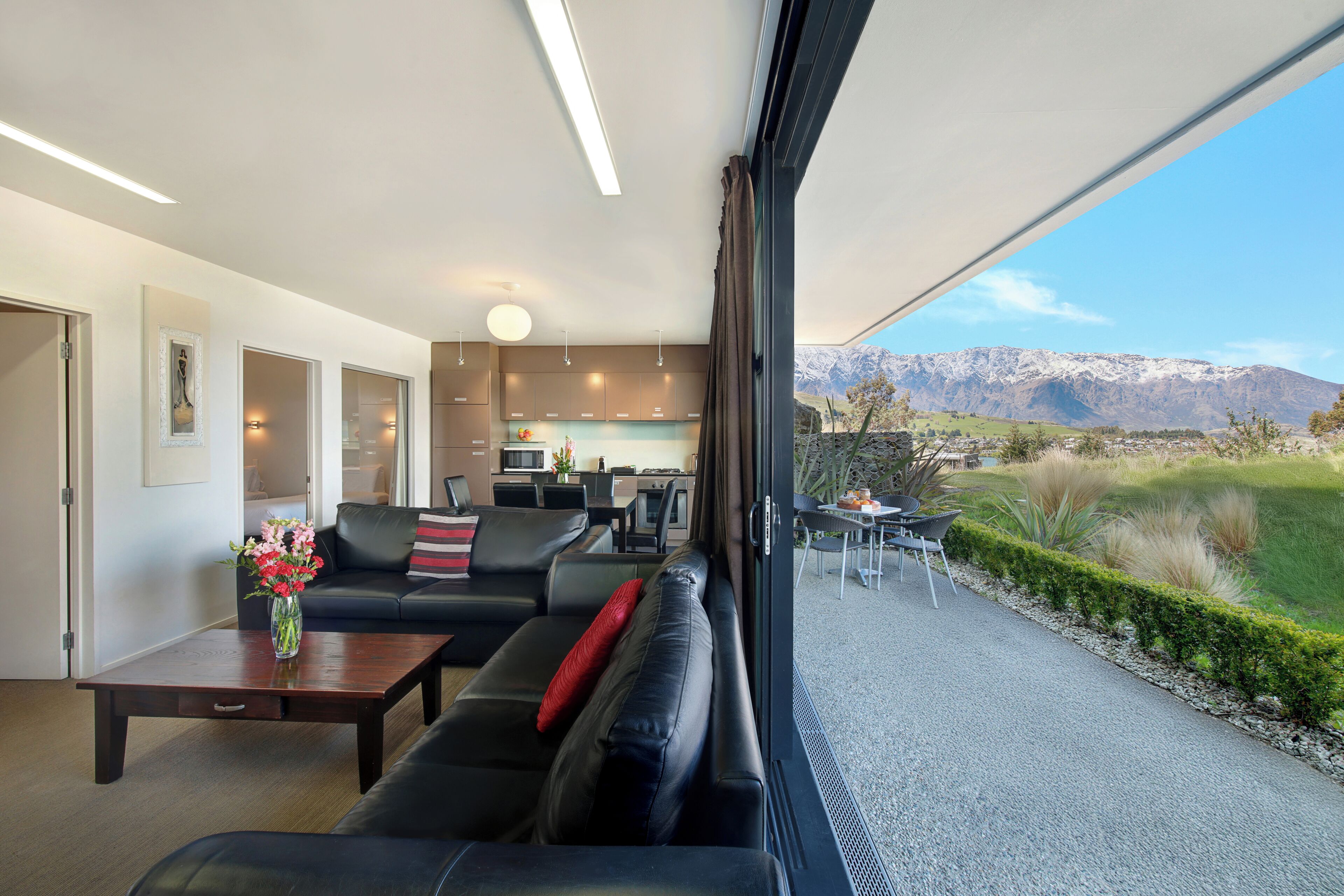 A modern living room with a sofa, coffee table, and a view of a kitchen and mountains.