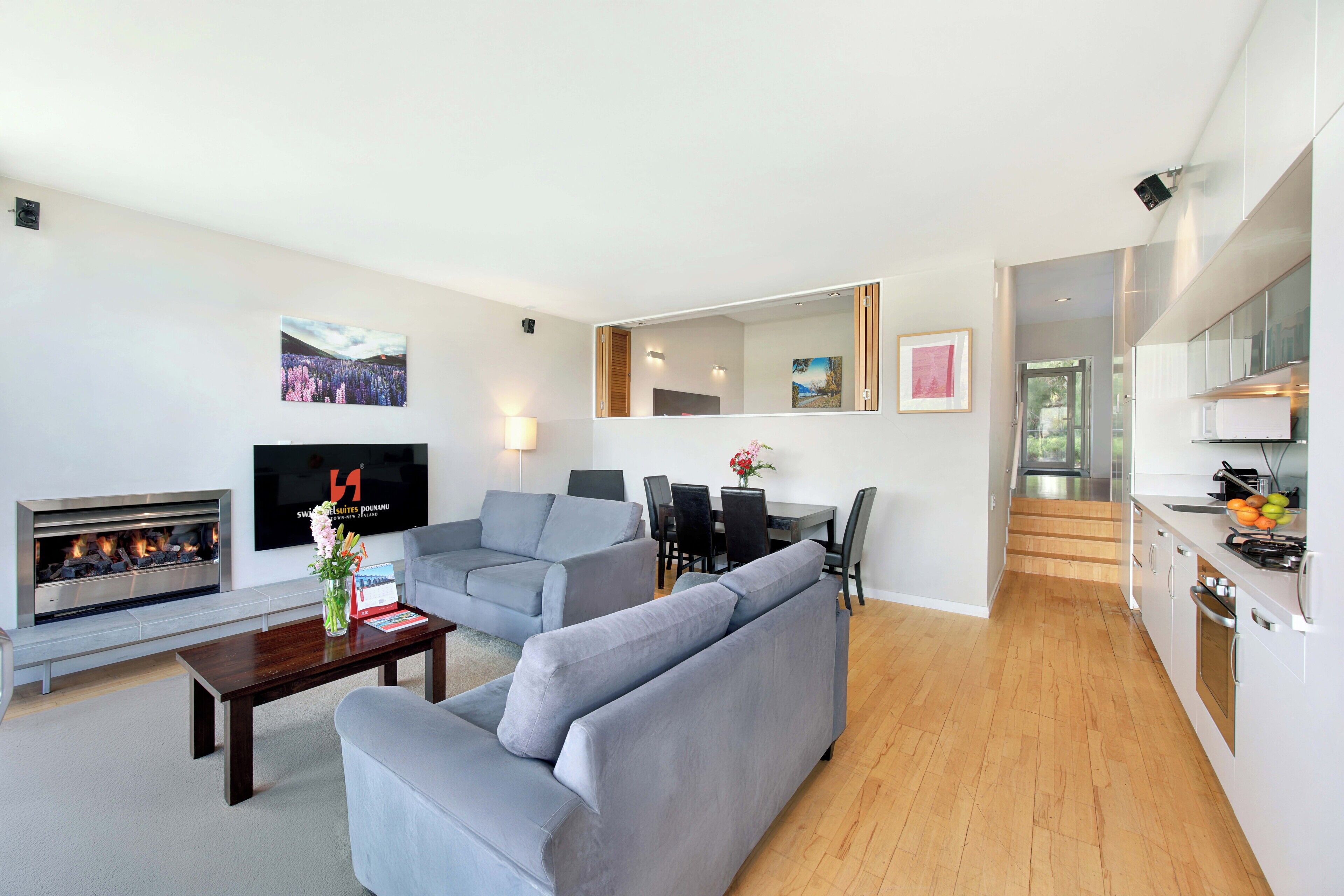 A modern living room with a fireplace, grey sofas, a dining area, and a kitchen with wooden flooring.