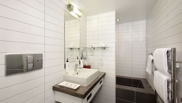 A modern bathroom with a white tiled wall, a wooden vanity, a large mirror, a built-in towel rack, and a separate shower area.