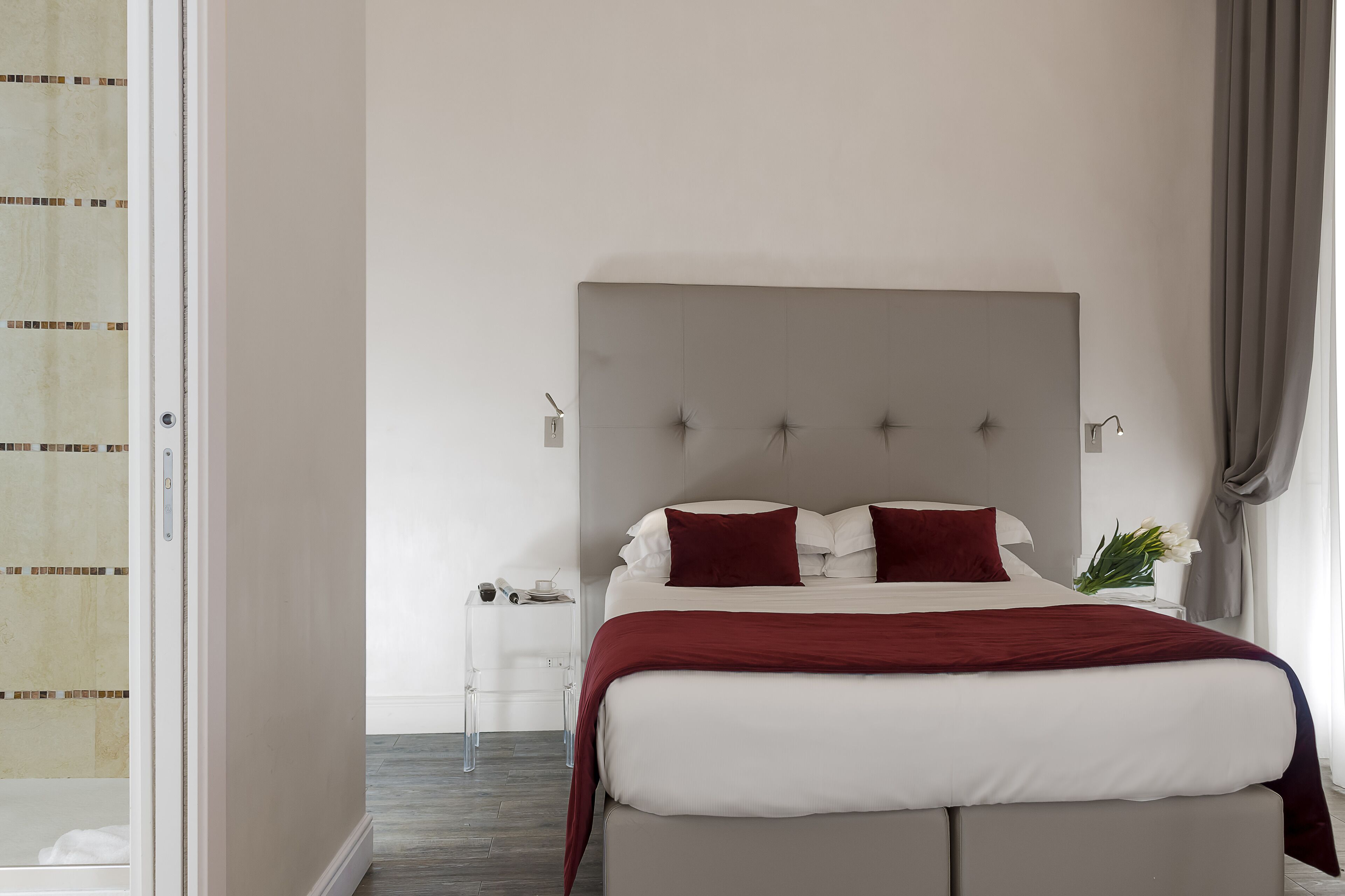 A bedroom with a bed, a nightstand, a bedside table, and a window with curtains.
