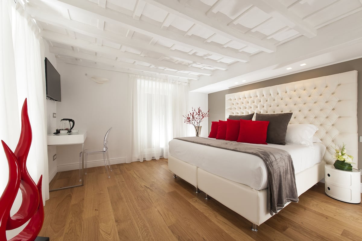 A modern bedroom with a large bed, a bedside table, a TV, and a red decorative chair.