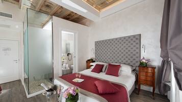 Un dormitorio moderno con ducha de vidrio, una cama grande con cabecera capitonada y una mesita de noche con un jarrón de flores.