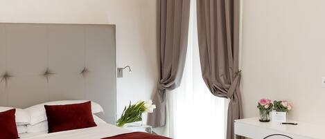 A hotel room with a bed, a desk, and a window with curtains.