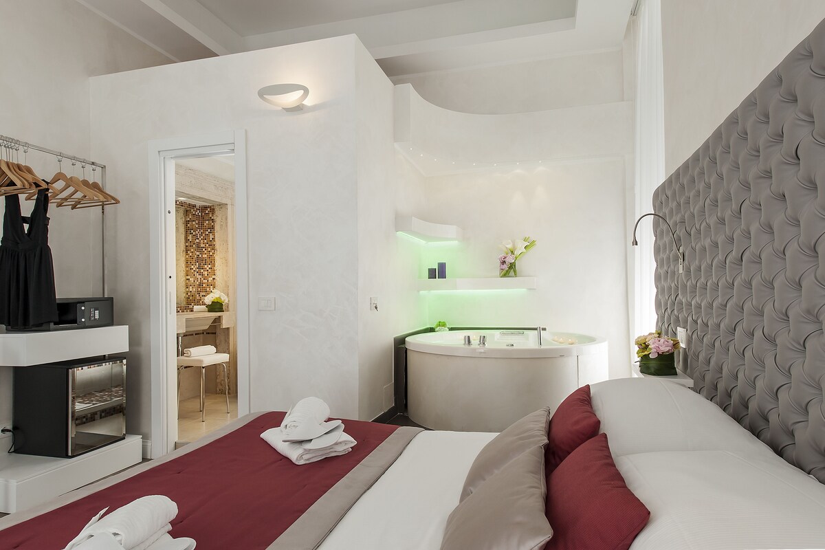 Et moderne hotelværelse med seng, et sminkebord med spejl, håndvask og et lille siddeområde.