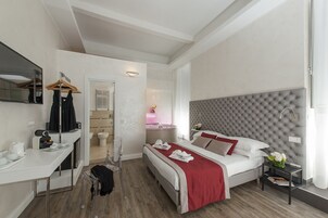 A modern hotel room with a bed, bedside table, and a desk with a chair.