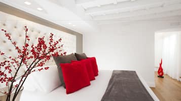 A modern hotel room with a tufted headboard, a bed with red and grey bedding, and a decorative red vase.
