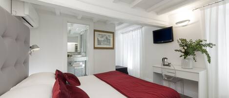 A modern hotel room with a large bed, a desk, a TV, and a plant.
