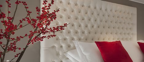 A bedroom with a tufted headboard, white bedding, and a vase with red berries.
