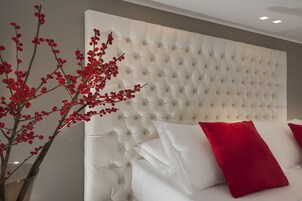Una camera da letto con testiera trapuntata, biancheria bianca e un vaso con bacche rosse.