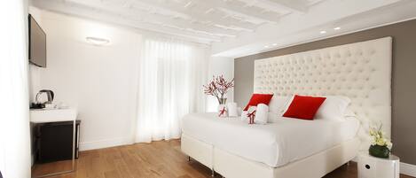 A modern bedroom with a large bed, a bedside table, a desk, and a TV mounted on the wall.
