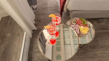 A room with a round table displaying two drinks with fruit garnishes, a plate with food items, and a decorative tray.