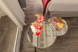 A room with a round table displaying two drinks with fruit garnishes, a plate with food items, and a decorative tray.