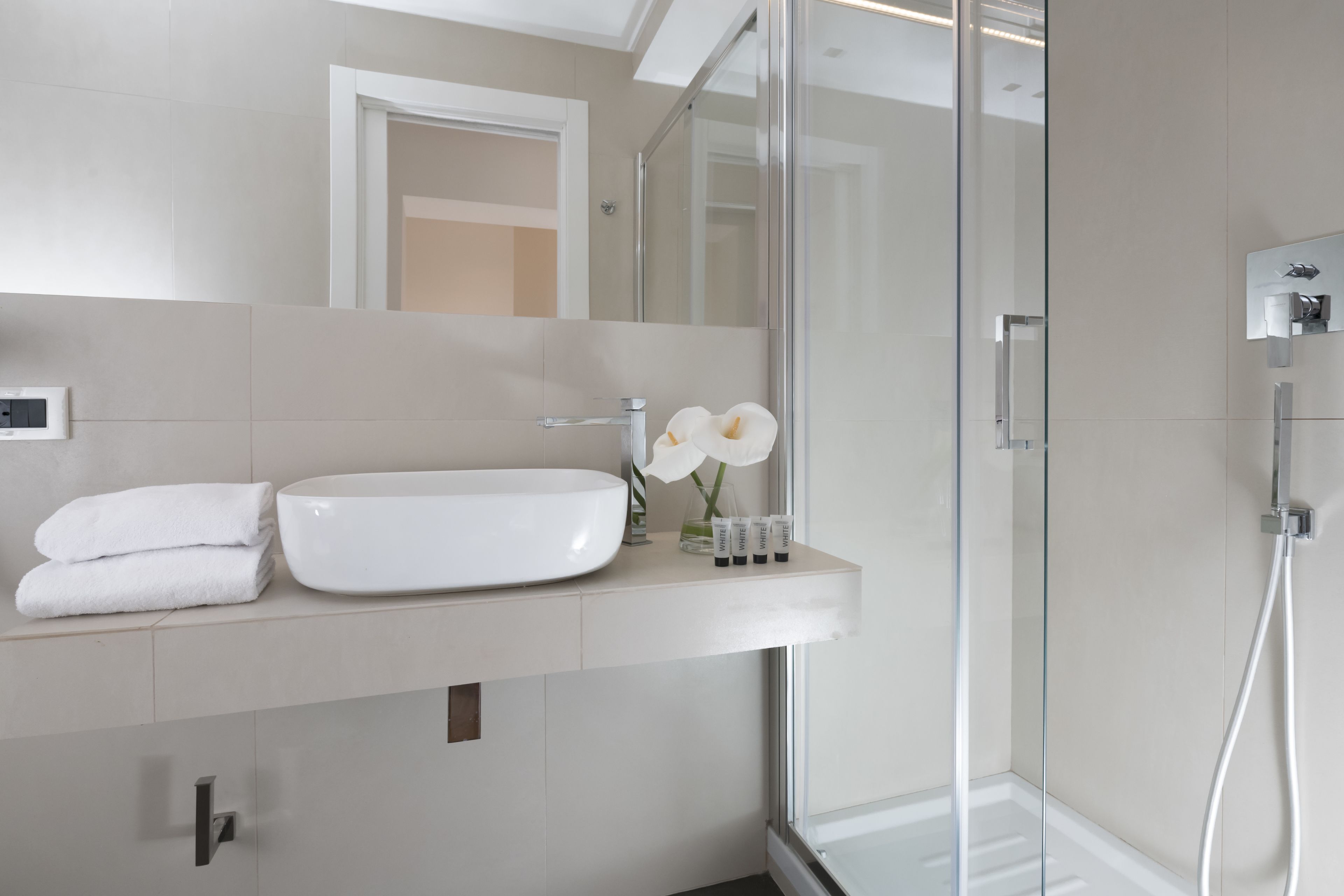 A modern bathroom with a white sink, glass shower enclosure, and a mirror above the sink.
