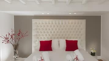 A neatly arranged hotel room with a tufted headboard, red and white pillows, a vase with red flowers, and neatly folded towels.