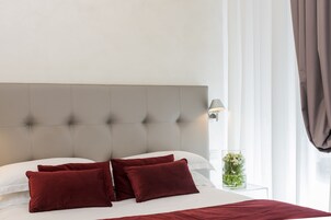 A neatly made bed with a tufted headboard, white linens, and two red pillows.