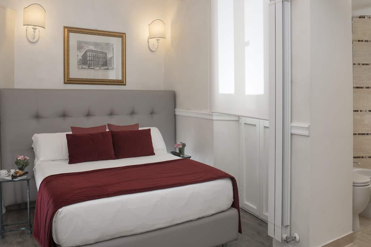 A hotel room with a large bed, two bedside lamps, a framed picture on the wall, and a view of the bathroom.