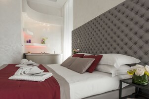 A modern hotel room with a large bed, a grey tufted headboard, and a bedside table with a vase of flowers.
