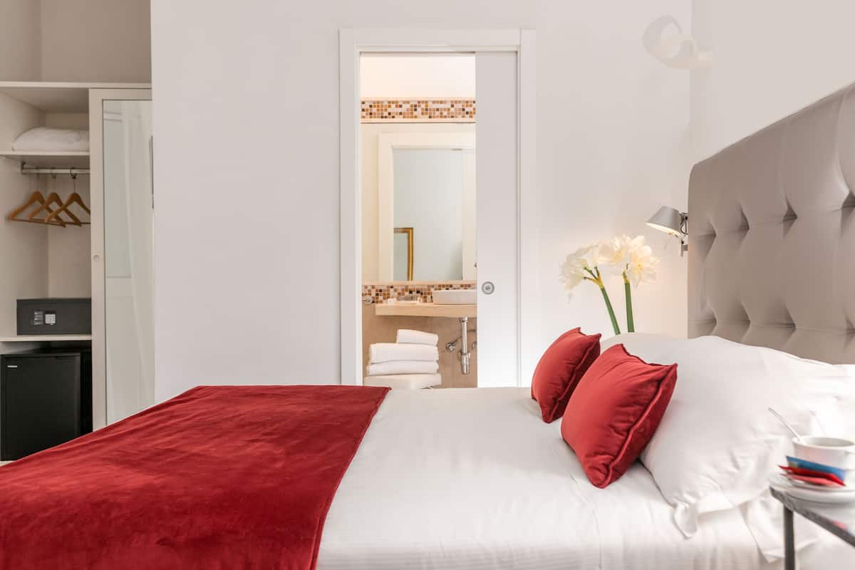 A hotel room with a bed, a wardrobe, a mirror, and a bathroom visible through an open door.