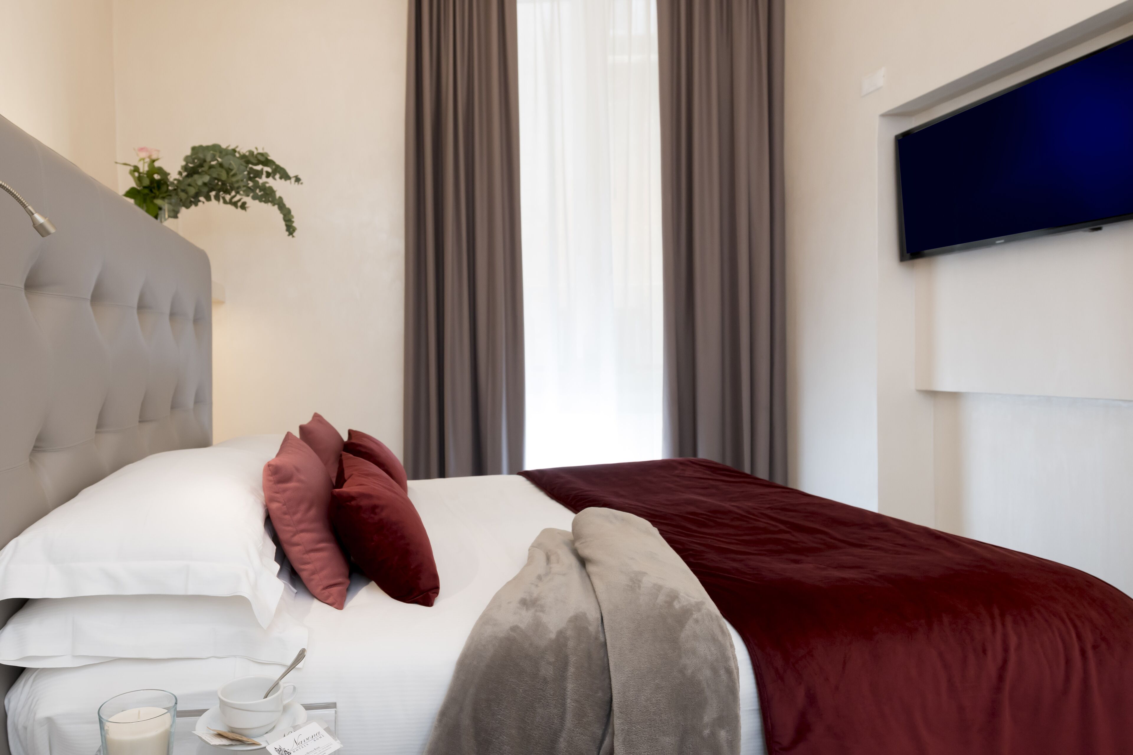 A neatly made bed with white and maroon pillows, a grey headboard, and a red blanket.