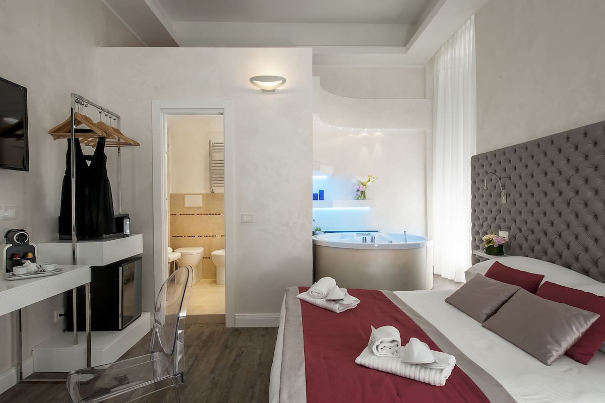 A modern hotel room with a bed, a desk, a chair, a hanging clothes rack, a bathroom, and a bathtub.