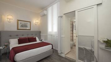 Un dormitorio moderno con una cama grande, una mesita de noche, un cuadro enmarcado y un baño visible a través de una puerta abierta.
