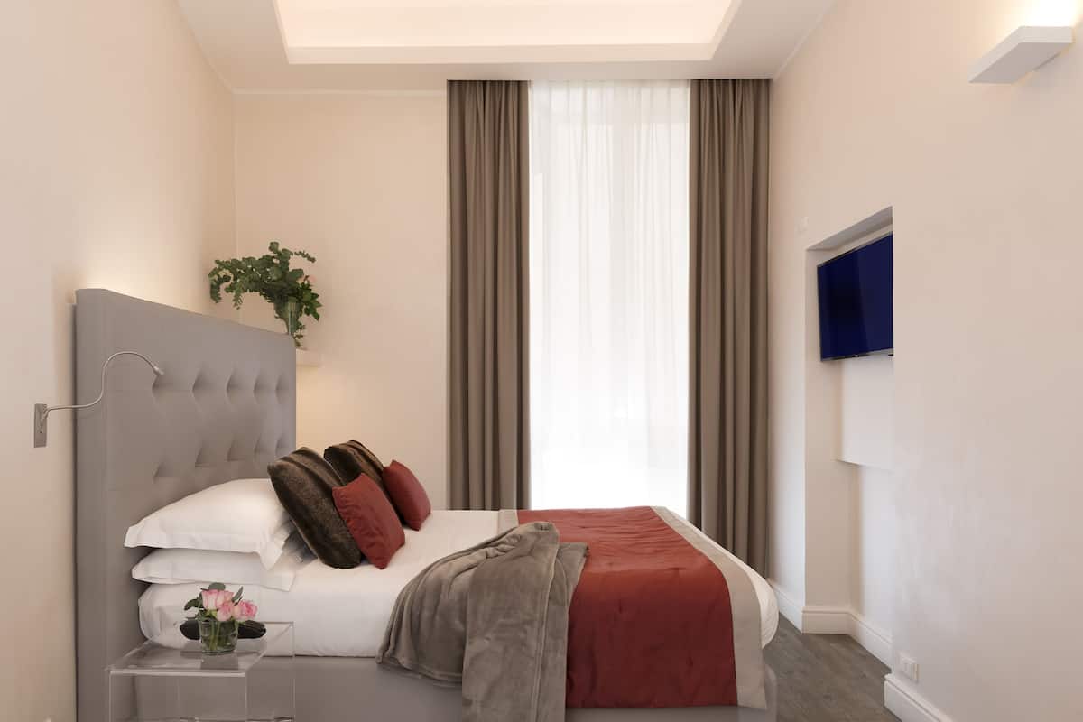 A modern bedroom with a large bed, a bedside table with a vase, and a TV mounted on the wall.