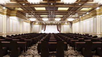 A conference room with rows of tables and chairs, a patterned carpet, and a chandelier ceiling.