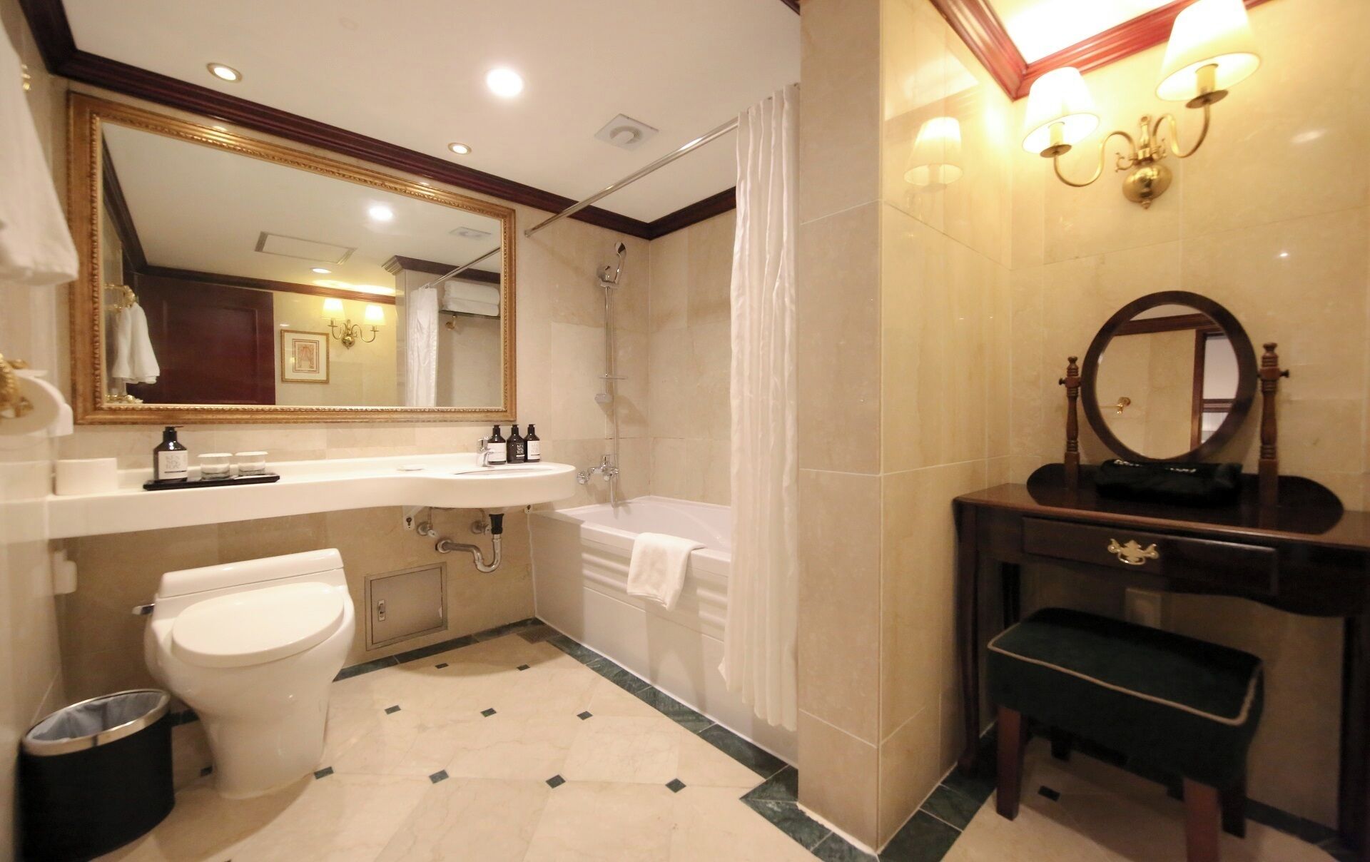 Un baño con inodoro, lavamanos, bañera, tocador con espejo y un banco.