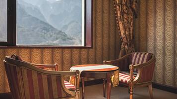 Habitación con una ventana grande que ofrece vistas a la montaña, dos sillones tapizados con estampado a rayas y una pequeña mesa de madera.