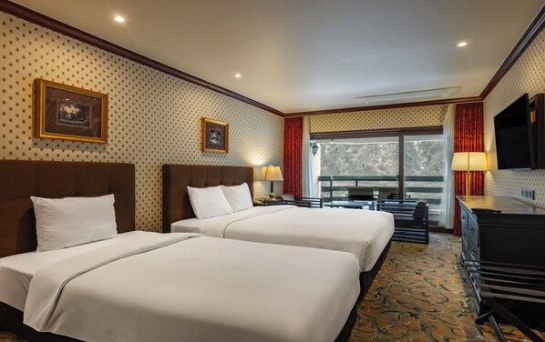 Habitación de hotel con dos camas, un escritorio, un televisor y un balcón con vistas.