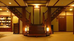 A grand staircase with wooden railings and a central light fixture, leading to a landing with a wooden door and a small table.