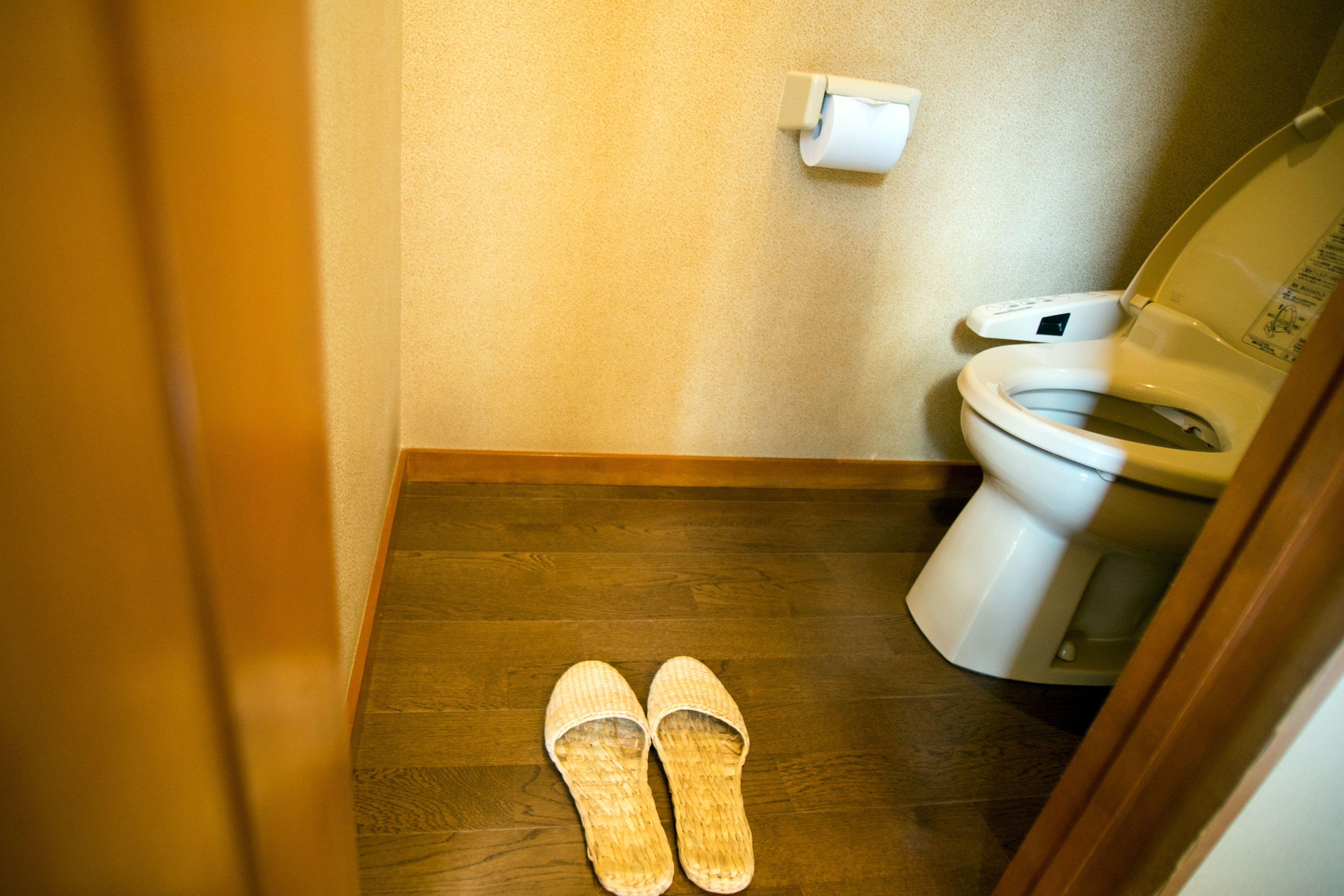 A bathroom with a wooden floor, a toilet, and a pair of slippers.