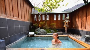 A hot spring area with a wooden deck, a stone lantern, and a small waterfall feature.