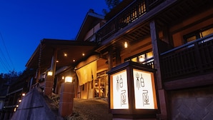 A traditional Japanese building with a wooden exterior, a covered entrance, and illuminated signage with Japanese characters.