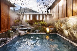 Un onsen japonais traditionnel, avec un bain en pierre entouré de structures en bois et offrant une vue sur une montagne.