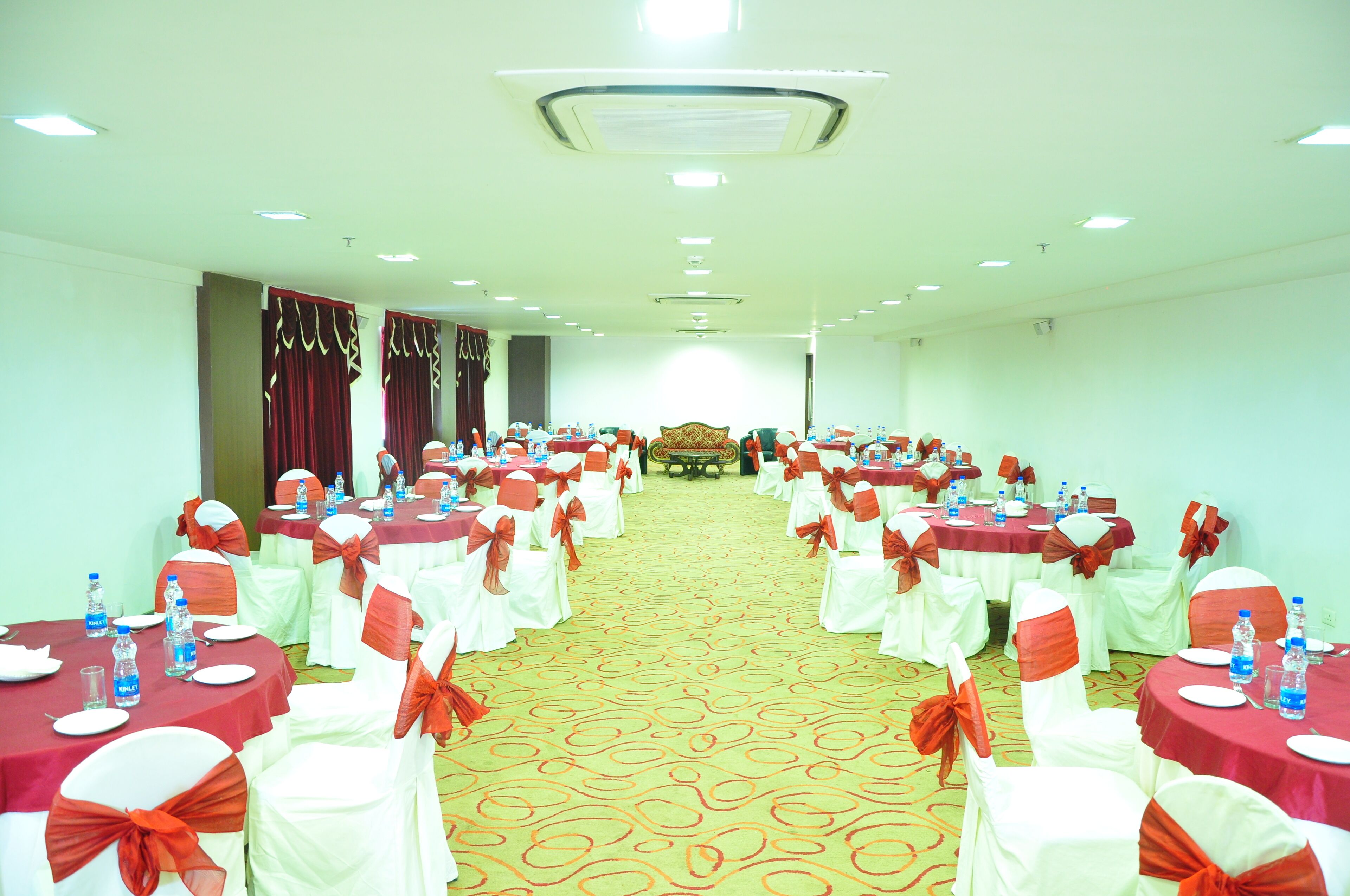 A conference room with round tables, white chairs with orange sashes, and a carpeted floor.