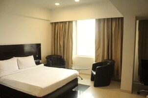Quarto de hotel com uma cama grande, uma mesa pequena, duas cadeiras e uma televisão.