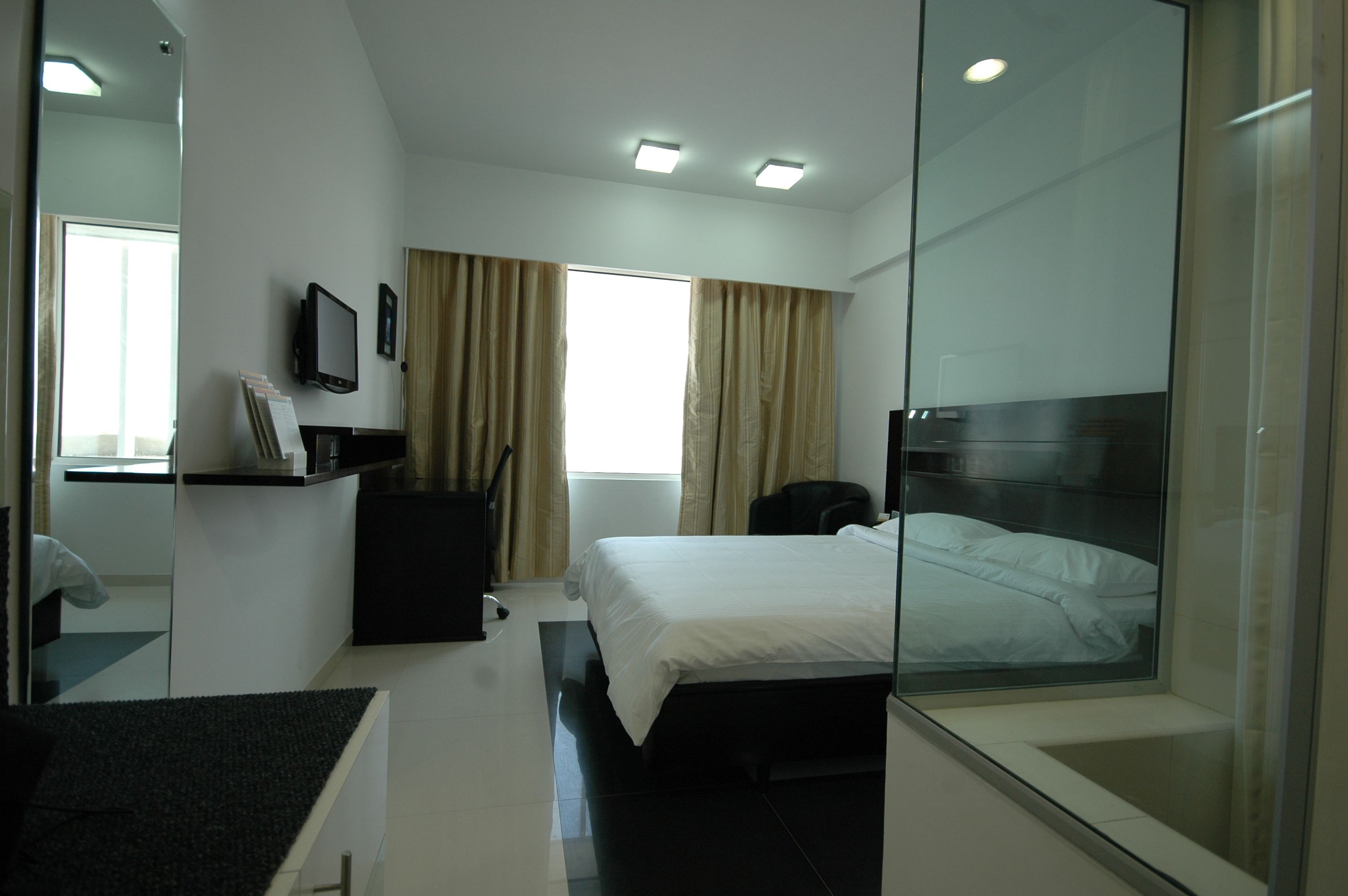 Una habitación de hotel moderna con cama, escritorio, silla, televisión y ventana con cortinas.