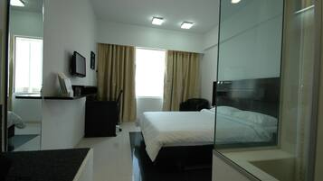 Una habitación de hotel moderna con cama, escritorio, silla, televisión y ventana con cortinas.