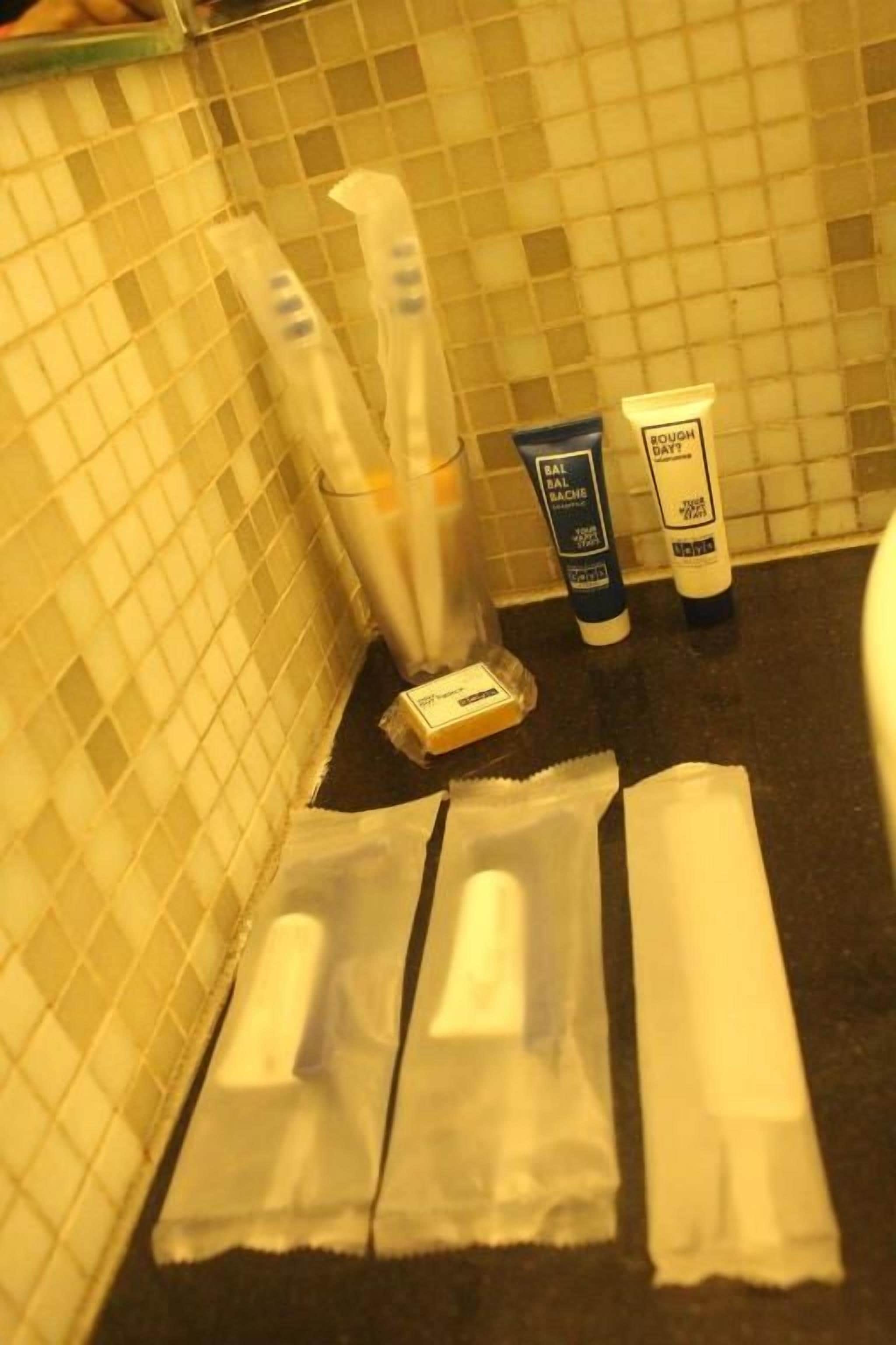 Un baño con pared de azulejos, un espejo y artículos de aseo que incluyen un cepillo de dientes, pasta de dientes y un rastrillo.