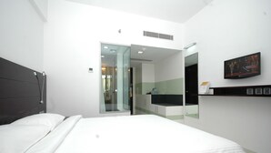 A modern hotel room with a large bed, a glass door leading to a bathroom, a mounted TV, and a small shelf with toiletries. - Keys Select by Lemon Tree Hotels, Ludhiana (Ludhiana)