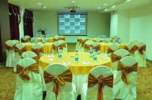 Un salón de conferencias con mesas redondas, sillas blancas con cintas marrones y una pantalla de proyector al fondo.