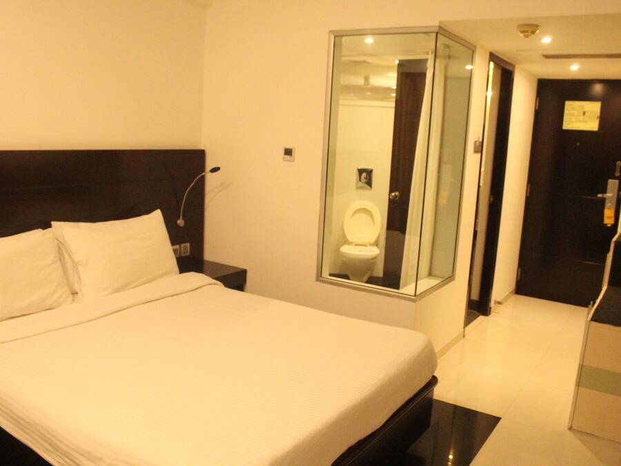 A hotel room with a large bed, a glass-enclosed bathroom, and a separate door leading to the bathroom.
