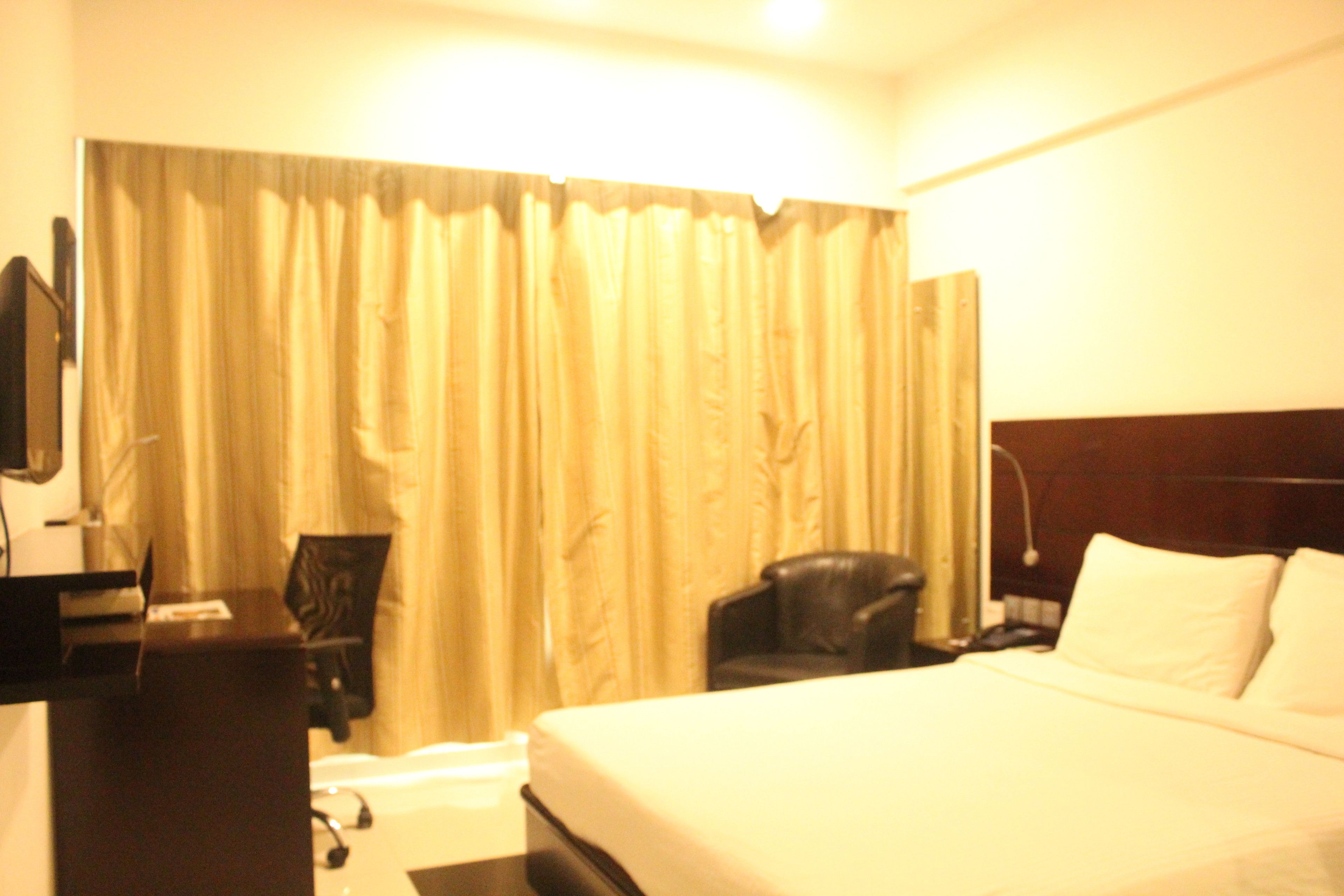 Una habitación de hotel con una cama, un escritorio con una computadora, una silla y una cortina.