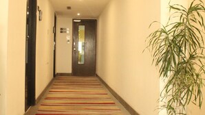 A hotel hallway with a carpeted floor, a potted plant, and a door at the end. - Keys Select by Lemon Tree Hotels, Ludhiana (Ludhiana)
