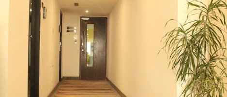 Un pasillo de hotel con piso alfombrado, una planta en maceta y una puerta al final.