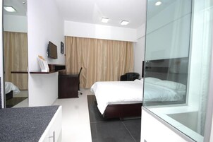 Una habitación de hotel moderna con cama, escritorio, silla, televisor y una pared divisoria de vidrio.