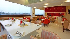A modern restaurant with a high ceiling and large windows. Tables are arranged in a spacious layout with striped chairs. - Keys Select by Lemon Tree Hotels, Ludhiana (Ludhiana)