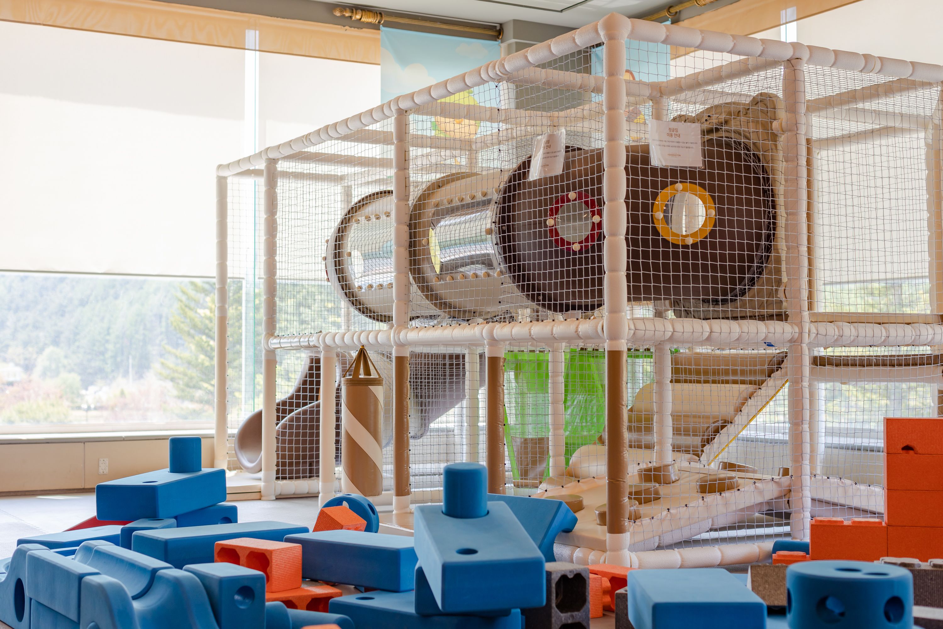 A play area with a playpen, various toys, and a window with a view of greenery.