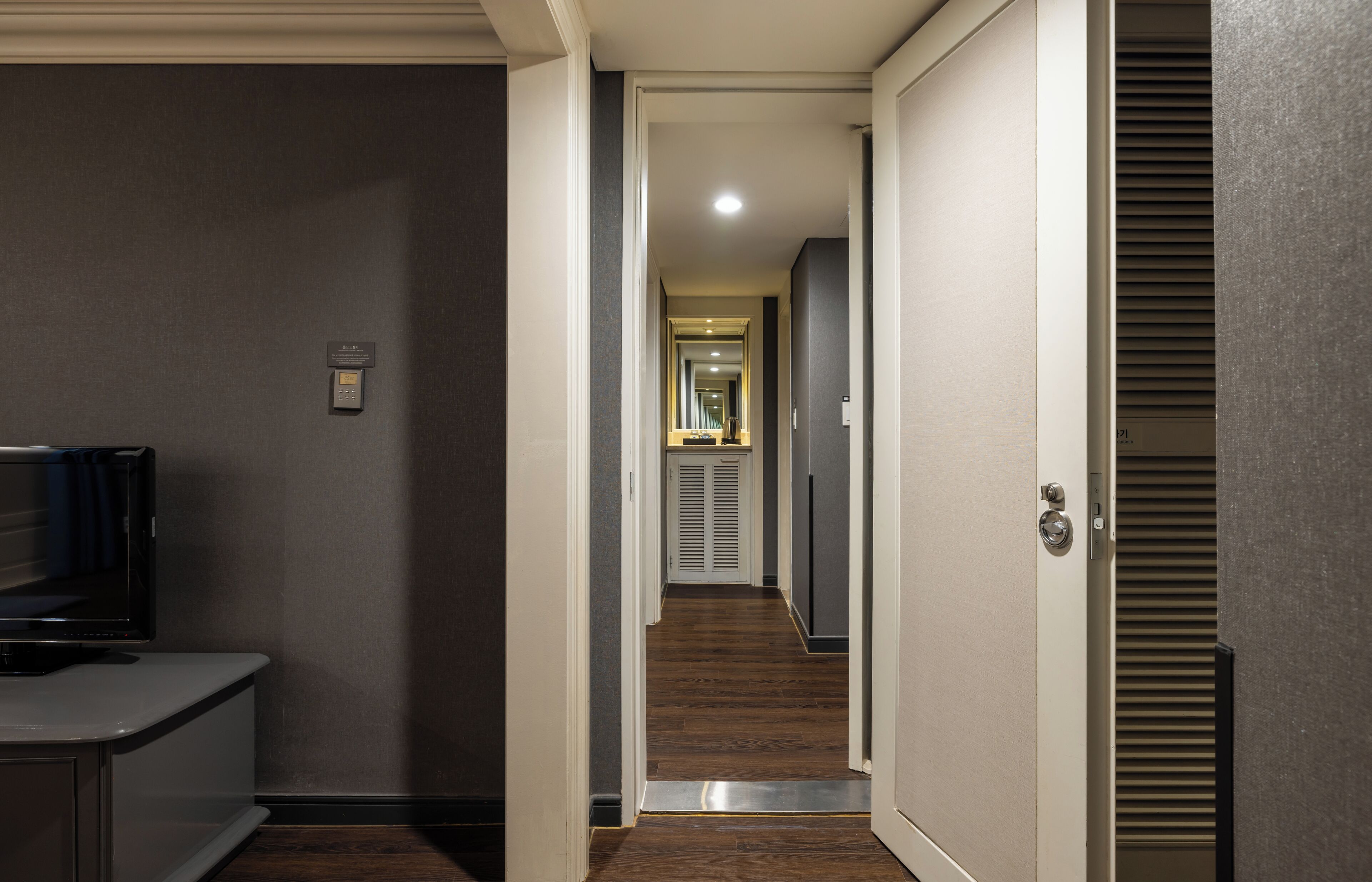A hallway with a television on the left, a door on the right, and a mirror at the end.